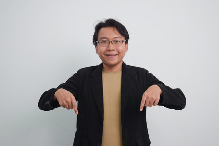 Joyful asian businessman with suit and casual shirt showing product or pointing gesture in isolated white backgroundの写真素材