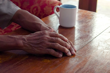hands of senior elder on table, old man in living room with his coffee glass with window viewの写真素材