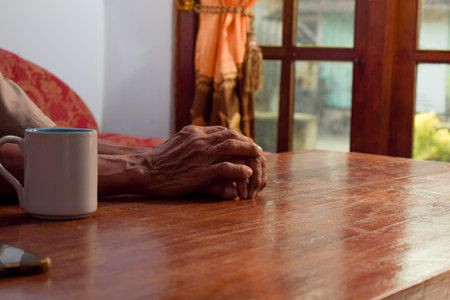 two hand of senior elder on table, loneliness old man in living room with his coffee glass with window viewの写真素材