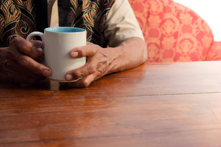 two hand of senior elder on table, loneliness old man in living room with his coffee glass with...