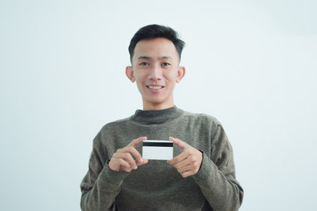 Joyful asian young men wear sweater and holding blank white credit card over white background
