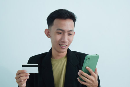 Joyful asian young businessman wear suit with tshirt holding blank white credit card and smartphone...