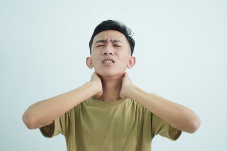 Close up asian young man touching neck in neckache or pain isolated on white backgroundの写真素材