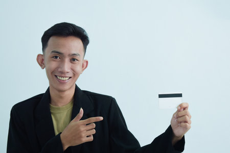 Joyful asian young businessman wear suit with tshirt and holding blank white credit card over white backgroundの写真素材
