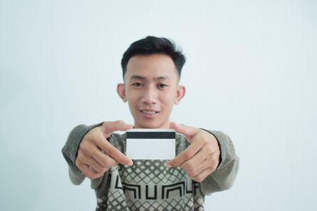 Joyful asian young men wear sweater and holding blank white credit card over white backgroundの写真素材