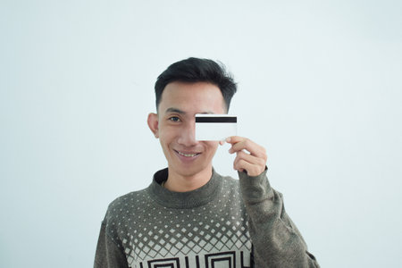 Joyful asian young men wear sweater and holding blank white credit card over white background