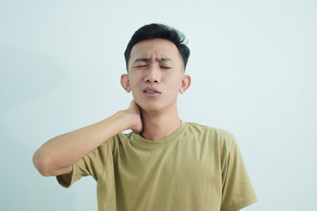 Close up asian young man touching neck in neckache or pain isolated on white backgroundの写真素材