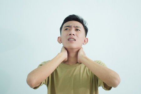 Close up asian young man touching neck in neckache or pain isolated on white backgroundの写真素材