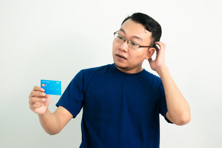 Thoughtful asian man hold and pointing credit card. Banking, Financial isolated, blue color concept.の写真素材