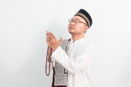 Asian Muslim man wearing white clothes doing praying hand pose during Ramadan Eid Al Fitr and eid adha days celebration isolated white background. Islamic celebration concept.の写真素材