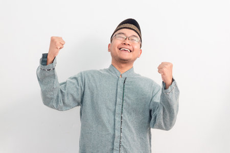 Asian Muslim man smiling doing successful gesture in Ramadan Eid Al Fitr and eid adha days celebration isolated white background. Islamic celebration concept.の写真素材
