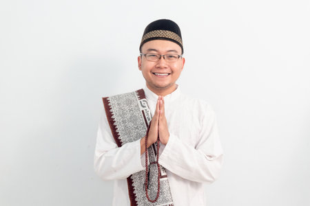 Asian Muslim man wearing white clothes doing praying hand pose during Ramadan Eid Al Fitr and eid adha days celebration isolated white background. Islamic celebration concept.の写真素材