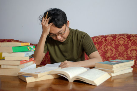 Asian young male reading book with frustrated gesture. Asian male with glasses confused face with...