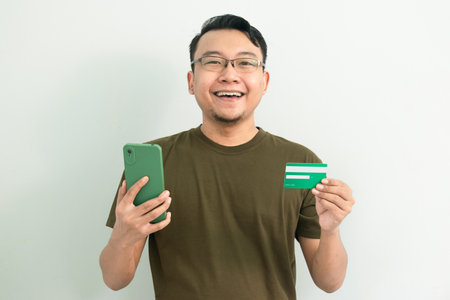 Happy asian man hold credit card and phone. Banking, Financial and technology isolated, green color...