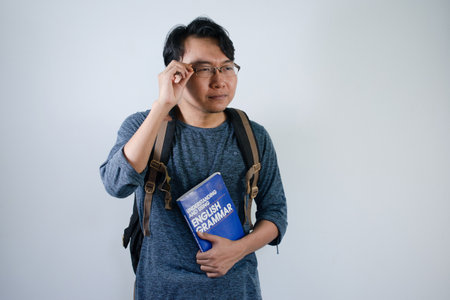 Asian male student wearing bag and holding book smiling and hand on glasses. Isolated white...