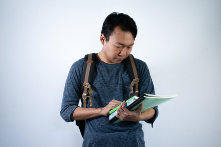 Asian young male student wearing bag and carrying books smiling and happy expression with isolated...