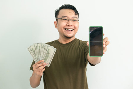 Happy asian man hold Money and showing phone screen. Banking, Financial and technology isolated, green color concept.の写真素材