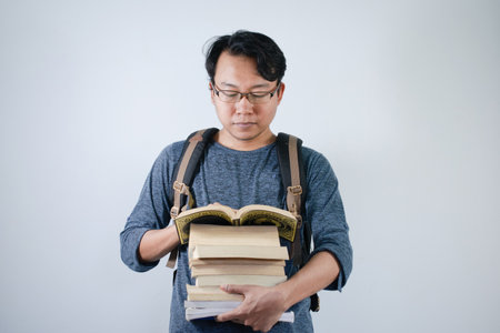 Asian young male student wearing bag and carrying books smiling and happy expression with isolated white backgroundの写真素材