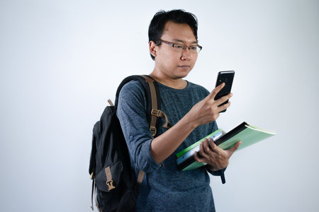 Asian young male student wearing bag have chatting or massage with the phone. isolated white backgroundの写真素材