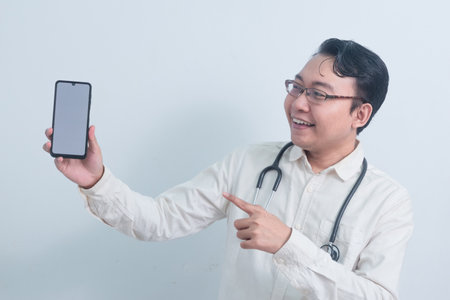 happy Asian man doctor, male nurse Pointing and showing phone isolated white background.の写真素材
