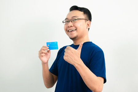 Happy asian man hold credit card with thumb up pose. Banking, Financial isolated, blue color concept.の写真素材