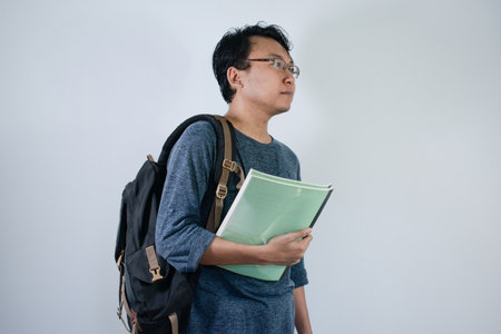 Asian young male student wearing bag and carrying books smiling and happy expression with isolated white backgroundの写真素材