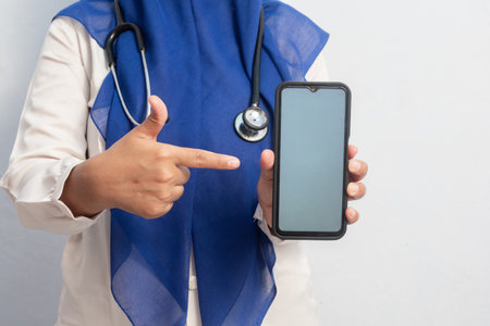 Muslim Female asian doctor or nurse holding phone and presenting hand pose. Isolated white background. Medical, healthcare and nurse concept.の写真素材