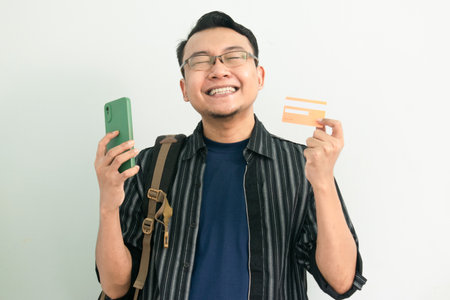 Happy asian Student hold credit card and phone with celebrating pose. Banking, Financial and technology isolated concept.の写真素材