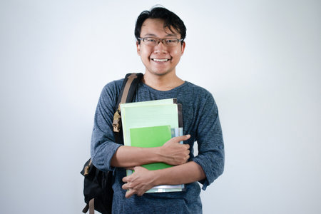 Asian young male student wearing bag and carrying books smiling and happy expression with isolated white backgroundの写真素材