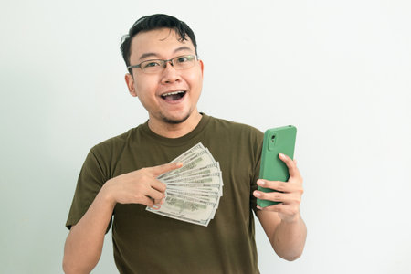 Happy asian man hold Money and pointing phone. Banking, Financial and technology isolated, green color concept.の写真素材
