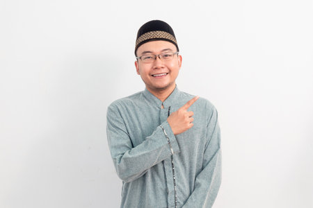 Asian Muslim man smiling doing pointing gesture in Ramadan Eid Al Fitr and eid adha days celebration isolated white background. Islamic celebration concept.の写真素材