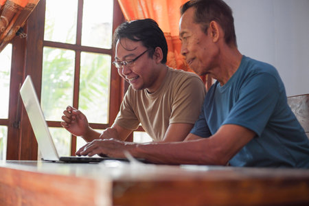 Happy adult son teaching old father using laptop. Young and senior togetherness conceptの写真素材