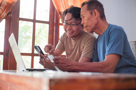 Happy adult son and old father pay online using laptop and credit card. Young and senior togetherness conceptの写真素材
