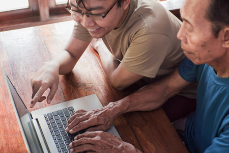 Happy adult son teaching old father using laptop. Young and senior togetherness conceptの写真素材
