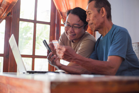 Happy adult son and old father pay online using laptop and credit card. Young and senior togetherness conceptの写真素材