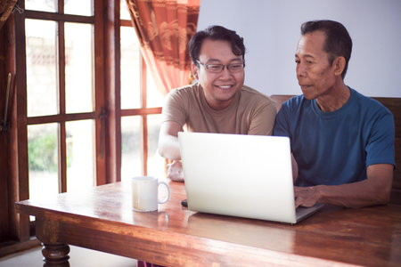 Happy adult son teaching old father using laptop. Young and senior togetherness conceptの写真素材
