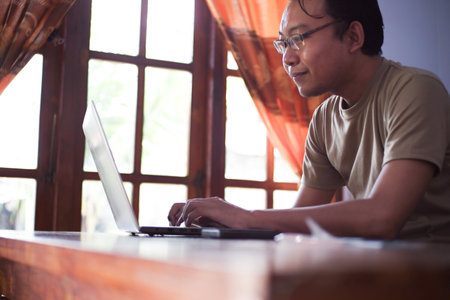 Asian Male with shirt working from home in living room with book, laptop and cup of coffee. Freelancer work at home conceptの写真素材