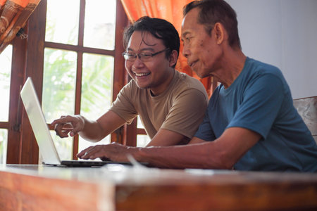 Happy adult son teaching old father using laptop. Young and senior togetherness conceptの写真素材