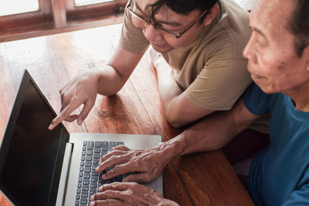 Happy adult son teaching old father using laptop. Young and senior togetherness conceptの写真素材