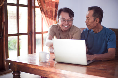 Happy adult son teaching old father using laptop. Young and senior togetherness conceptの写真素材