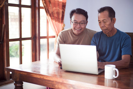 Happy adult son teaching old father using laptop. Young and senior togetherness conceptの写真素材