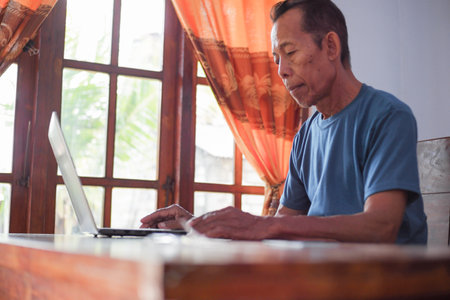 Asian old man with shirt using laptop in living room. Senior and technology conceptの写真素材