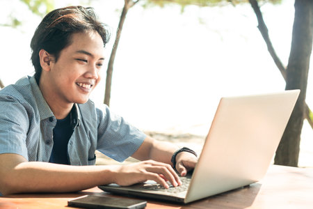 Happy Asian Young businessman work at outdoor with laptop. Concept of remote and freelance work. Young successful man wearing casual blue cloth.の写真素材