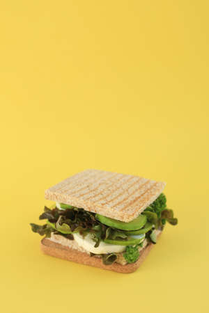 A tasty green vegan sandwich with avocado. lettuce, parsley, mozzarella on toasted bread placed on yellow background.の写真素材