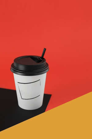Recyclable white paper cup for coffee, tea, cappucino and other hot beverage with black plastic cover and tube on red and yellow and black geometric background.の写真素材