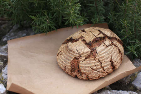 Bio whole grain homemade bread made on sour dough laying on kraft paper on stone curb near rosemary, shot in rustic style.の写真素材