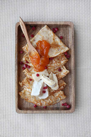 Homemade pancakes with apricot jam, fresh brie cheese and red currant on wooden plate with wooden spoon. Top view.の写真素材
