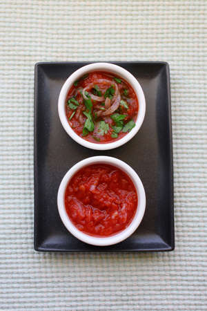 Tomato sauce or marinade for meat and bbq with onion and herbs. Ceramic white bowls and rectangular dark gray plateの写真素材