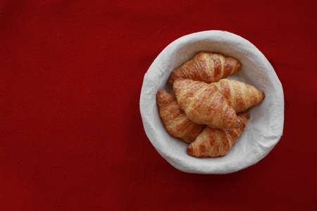 Five freshly baked tasty crusty croissants in a basket on red tablecloth .の写真素材