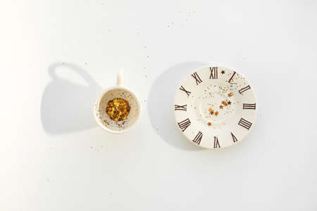 Empty cup of coffee with tinsel and decorating golden stars inside. small saucer with clock face icon. White background.の写真素材
